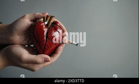 Die Hände der Frau halten ein Modell eines kleinen Herzens auf ihren Handflächen, Nahaufnahme, Zigaretten liegen neben ihnen Stockfoto