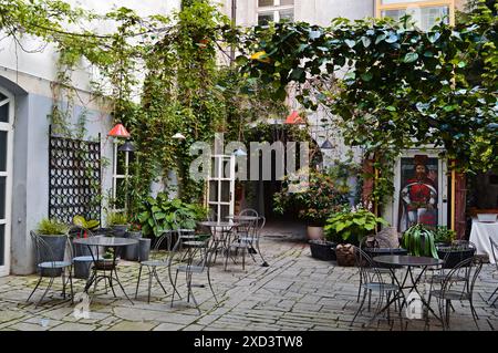 Eine hübsche Terrasse mit Bistrotischen und -Stühlen und ein Efeu-überdachtes Gebäude in einer Altstadt in Europa. Stockfoto