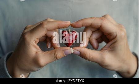 Die Hände der Frau halten ein Modell eines kleinen Herzens auf ihren Handflächen, Nahaufnahme, Zigaretten liegen neben ihnen Stockfoto