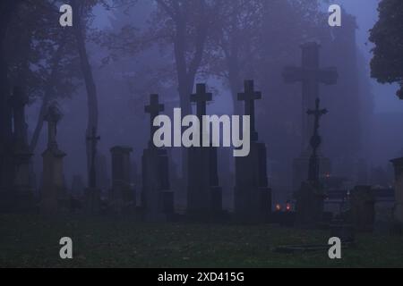 Gräber und Kreuze unter Bäumen mit einer schrecklich nebeligen Atmosphäre auf einem mitteleuropäischen Friedhof Stockfoto