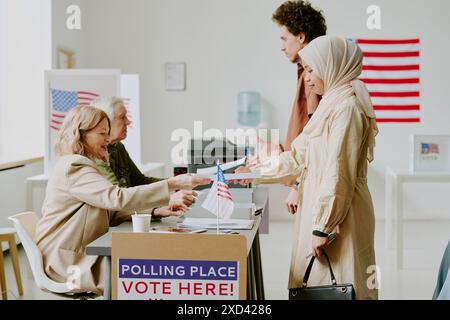 Birassischer junger Mann und Frau im Hijab, die am Wahltag Stimmzettel am Wahllokal abgeben, Seitenansicht Stockfoto