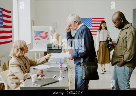 Seitenaufnahme eines älteren kaukasischen Mannes, der am Wahltag Wahlzettel zur Abstimmung nimmt Stockfoto