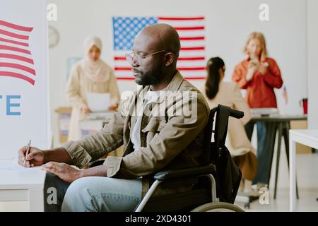 Mittelgroßer Schuss eines behinderten Afroamerikaners, der am Wahllokal Stimmzettel einfüllte Stockfoto