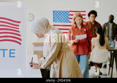 Junge muslimische Frau mit Hijab, die am Wahltag in der Wahlurne für den Kandidaten stimmte Stockfoto