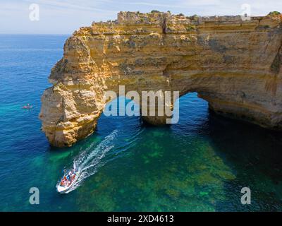 Ein großes Boot führt unter natürlichen Bögen aus Felsen in kristallklarem Wasser an der Küste vorbei, aus der Vogelperspektive, Praia da Marinha, doppelter Felsbogen, Lagoa Stockfoto