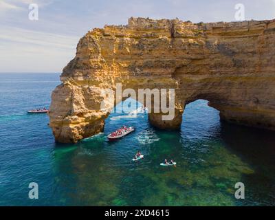 Großer Felsbogen im blauen Wasser der Algarve, Portugal, mit mehreren Booten und Touristen in der Gegend, aus der Vogelperspektive, Praia da Marinha, Doppelfelsen Stockfoto