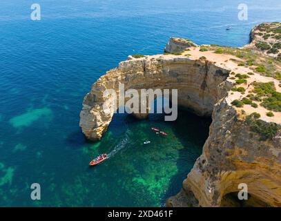 Natürliche Bogenformationen an der Küste, umgeben von klarem Wasser mit Booten, die darunter vorbeifahren, aus der Vogelperspektive, Praia da Marinha, doppelter Felsbogen Stockfoto