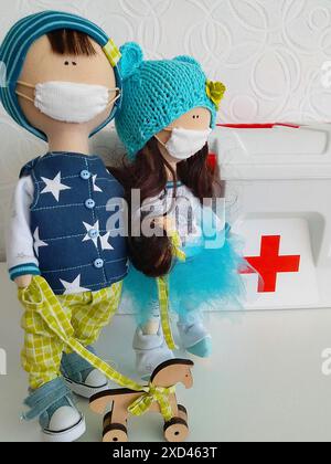 Zwei Puppen mit Gesichtsmasken, blau und grün gekleidet mit einem Gesundheitsthema, neben einer medizinischen Box mit einem roten Kreuz Stockfoto