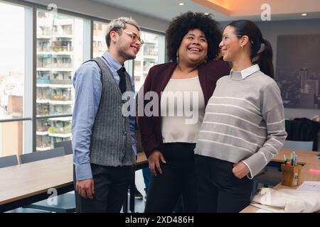 Kollegen, junge Leute im Büro lachen sich gegenseitig aus. Es sind zwei Frauen und ein Mann unterschiedlicher ethnischer Herkunft, die drei sind Latinos und sie sind A Stockfoto