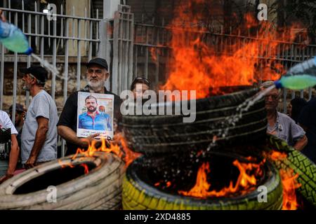 Beirut, Libanon. 20. Juni 2024, Beirut, Beirut, Libanon: Vater von Ahmad al-Kaadan, der bei der massiven Explosion des Hafens am 5. August 2020 ums Leben kam, trägt sein Bild hinter brennenden Reifen im Justizpalast von BeirutÃ¢â‚¬â„¢während eines Protestes von Familien der Opfer der Explosion. Weniger als zwei Monate bis zum 4. Jahrestag der Explosion, bei der mehr als 200 Menschen ums Leben kamen, ist fast alles unbekannt Ã¢â‚¬ von der Person, die die Verbringung angeordnet hat, bis hin zu den wiederholten Warnungen der Beamten vor der Gefahr. Quelle: ZUMA Press, Inc./Alamy Live News Stockfoto