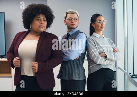 Porträt von drei Geschäftsleuten, zwei Frauen und einem Mann unterschiedlicher Ethnien und jungen Menschen, die mit überkreuzten Armen im Büro stehen und nach außen schauen Stockfoto