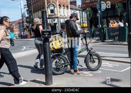 Männliche Essenslieferungen stehen an der Ampel und überprüfen an einem sonnigen Tag sein Navigationsgerät und Bestellungen im Stadtzentrum von Leeds Stockfoto