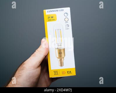 Paris, Frankreich - 15. Mai 2024: POV eines männlichen Hands mit einer neuen IKEA Lunnom LED-Lampe mit 21 W Leistung, 200 lm Intensität, vorgeschriebenem Etikett, 15 Stunden Betriebszeit und E14-Sockel, die Produktdetails vor einem einfachen Hintergrund hervorheben Stockfoto
