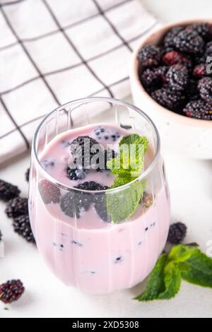 Maulbeershake, Smoothie oder Joghurtgetränk auf portioniertem Glas, mit vielen frischen Bio-Maulbeerbeeren und Minze, auf weißem Küchentisch, Kopierraum Stockfoto