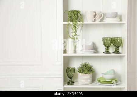 Verschiedene saubere Geschirr und Zimmerpflanzen auf den Regalen im Schrank drinnen Stockfoto