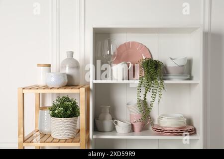 Verschiedene saubere Geschirr und Zimmerpflanzen auf den Regalen im Schrank drinnen Stockfoto