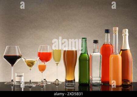 Flaschen und Gläser mit verschiedenen alkoholischen Getränken auf dem Tisch vor beigefarbenem Hintergrund Stockfoto