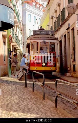 Touristen steigen in den alten Lissabon-Straßenbahnwagen Nr. 542, der sich durch die engen Gassen der portugiesischen Stadt windet, nur wenige Meter von den Häusern der Route 28 entfernt. Stockfoto