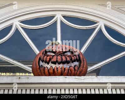 An einem Herbsttag in Salem Massachusetts hängt ein gruseliger Halloween-Kürbis mit einem bösartig aussehenden Jack-o-Laterne-Gesicht vor einem Fenster über einer Tür Stockfoto