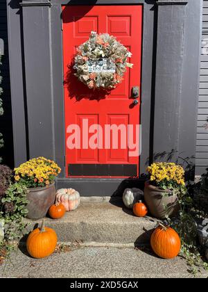 Ein Haus mit roter Haustür in Salem Massachusetts ist an einem sonnigen Herbsttag zu Halloween mit Herbstblumen, Kürbissen und einem Kranz dekoriert Stockfoto