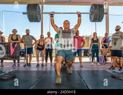 Athleten, die Gewichtheben bei einem intensiven CrossFit-Wettkampf in Sevilla, Spanien, durchführen. Die Massen beobachten die Teilnehmer und feuern sie an. Stockfoto