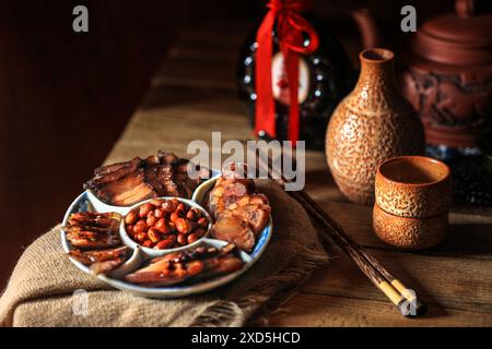 Traditionelle chinesische Wurst und Schweinefleisch, in Scheiben geschnitten auf einem antiken Teller, Erdnüsse in der Mitte für Wein trinken - dunkles und stimmungsvolles Stillleben Stockfoto