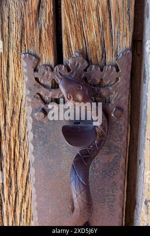 Schließen Sie die antike Mesquite-Holztür mit kunstvoll verzierten Schmiedeeisen-Verriegelung in Form einer Schlange an der Missionskirche San Xavier del Bac Stockfoto