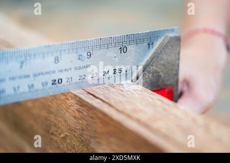 Nahaufnahme einer Person, die ein quadratisches Metalllineal verwendet, um ein Stück Holz zu messen, wobei der Schwerpunkt auf Präzision in der Holzbearbeitung liegt. Stockfoto