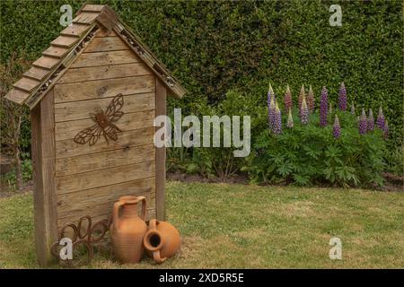 Übergroßes Insektenhaus mit Lipinen im Hintergrund und verschiedenen Gartenornamenten, darunter eine Biene und Pfotenmuster Stockfoto