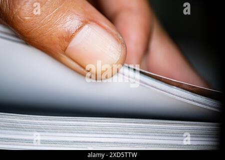 Nahaufnahme des Daumens einer Person, der durch die Seiten eines Buches oder einer Zeitschrift springt. Stockfoto