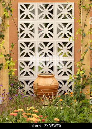 Terrakotta-Urnen-Wasserspiel, das an einer dekorativen Blockwand in einem britischen Garten mit orangefarbenen Blüten im Vordergrund steht Stockfoto