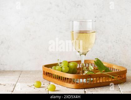 Stillleben mit einem Glas Weißwein mit Trauben und Traubenblättern auf einem Vintage-Korbtablett in der Küche. Essen und Trinken Konzept Stockfoto