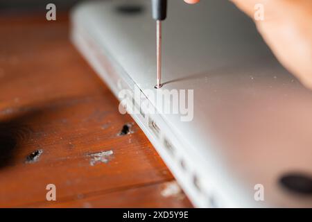 Nahaufnahme einer Person, die einen Laptop auf einem Holztisch mit einem Schraubendreher öffnet. Stockfoto