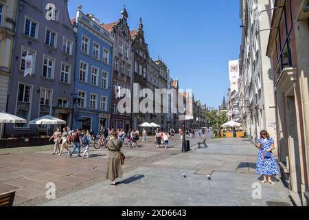 Touristen, die einen sonnigen Tag in der Długa-Straße in Danzig genießen, gesäumt von farbenfrohen historischen Gebäuden und Cafés im Freien. Stockfoto