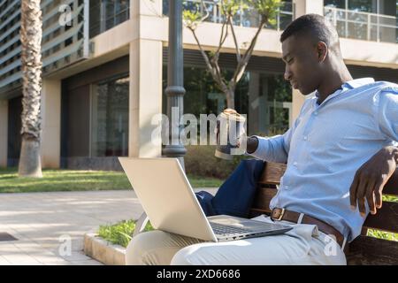 Aufmerksamer afroamerikanischer Profi, der draußen im Finanzviertel mit seinem Laptop arbeitet. Business-, Reflexion- und Produktivitätskonzept in Stockfoto