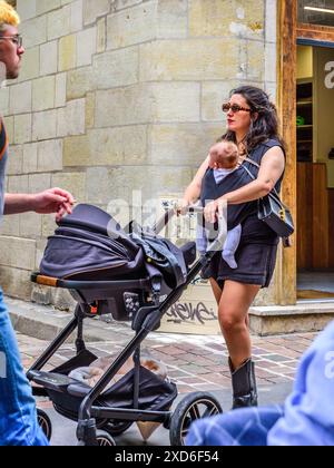 Junge, modische Mutter, die Baby trägt und die Kinderwagen schiebt, im Stadtzentrum - Tours, Indre-et-Loire (37), Frankreich. Stockfoto