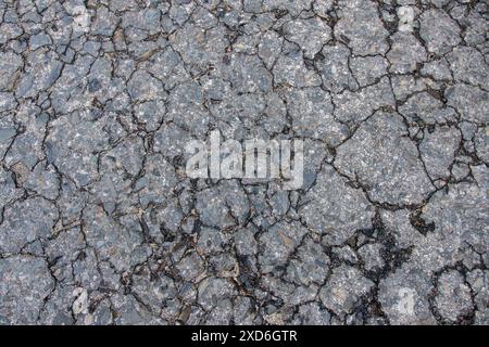 Nahaufnahme einer gerissenen Asphaltoberfläche mit detaillierter Textur und Verschleiß. Stockfoto