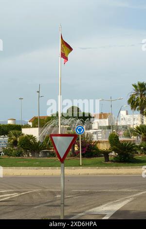 Almeria, Spanien - 25. Mai 2023: Eine spanische Flagge fliegt hoch über einem Kreisverkehr in Almeria, Spanien. Ein Ertragsschild steht in der Mitte des Kreisverkehrs, wi Stockfoto