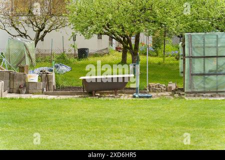 Eine alte Badewanne liegt auf dem Gras in einem üppigen Garten im Hinterhof. Stockfoto