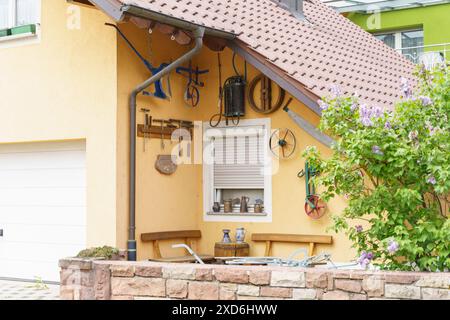 Ein gelbes Haus mit einem weißen Garagentor, einem Fenster mit einem weißen Rollladen und Werkzeugen, die an der Wand hängen. Ein Garten mit Blumen und einer Steinmauer Stockfoto