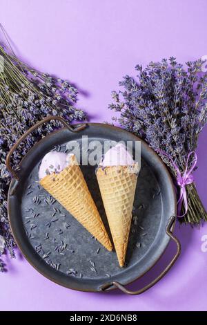 Zwei Lavendeleis in Waffle Cones auf einem Tablett und Blumensträuße aus trockenem Lavendel auf lila Hintergrund. Stockfoto
