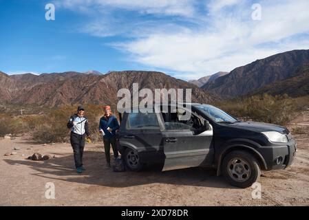 Zwei Reisende stehen neben ihrem Fahrzeug in einer bergigen Landschaft in einer wilden Gegend von Mendoza, Argentinien. Das Abenteuer, Urlaub zu genießen Stockfoto