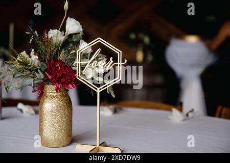 Hochzeitsempfang im Freien - Gäste-Tisch-Einrichtung. Goldene Glitzervase mit burgunderroten Pfingstrosen, Eukalyptusblätter Blumenarrangement Stockfoto