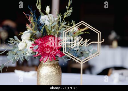 Hochzeitsempfang im Freien - Gäste-Tisch-Einrichtung. Goldene Glitzervase mit burgunderroten Pfingstrosen, Eukalyptusblätter Blumenarrangement Stockfoto