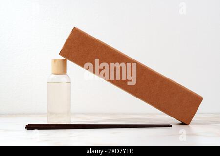Brauner Karton mit Glasflasche und Holzstäben auf weißer Oberfläche Stockfoto