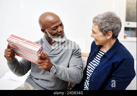 Überraschung, Sofa und reifes Paar mit Geschenk, um Geburtstag, Jubiläum oder Dankbarkeit zu Hause zu feiern. Liebe, glückliche Frau und Mann auf Couch mit Geschenk Stockfoto