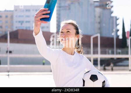 Frau, die Selfie mit dem Telefon macht und einen Ball hält Stockfoto