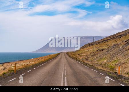 Straße in island, die um einen Hügel führt, mit hohen Bergen, Fjord, Meer, blauem Himmel, Sonnenschein, Klippen, auf der Straße 60 in den Westfjorden, Stockfoto