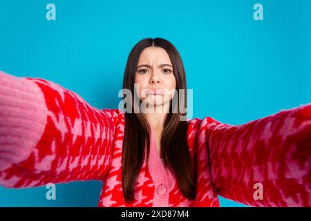 Foto von verärgerter düsterer Frau mit geradem Haar gekleideter Strickjacke, die Selfie-gegossene Lippen auf blauem Hintergrund isoliert macht Stockfoto