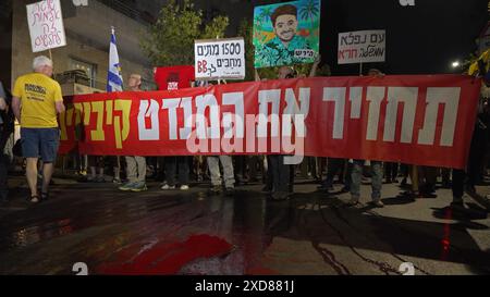 JERUSALEM – 20. JUNI: regierungsfeindliche Demonstranten halten Schilder, während sie über rot gefärbtem Wasser stehen, das sie auf die Straße gegossen haben, um israelische Geiseln zu symbolisieren, die während einer Demonstration in der Nähe der Privatresidenz des Premierministers getötet wurden, gegen Netanjahus Regierung und die Forderung nach Neuwahlen am 20. Juni 2024 in Jerusalem. Israel Stockfoto